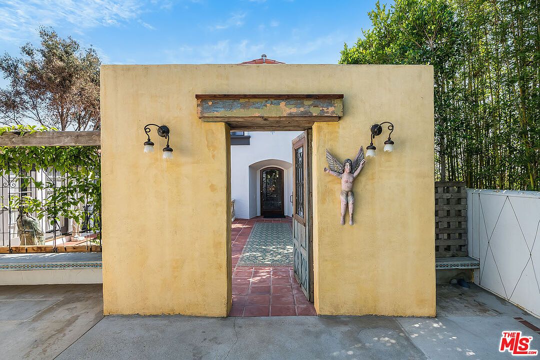 A sun-warmed ochre stucco threshold at 1046 Chautauqua, with twin lanterns flanking the open Spanish doors. A patinated cherub sculpture is mounted to the right; through the doorway, terracotta tile and an interior arch beyond.