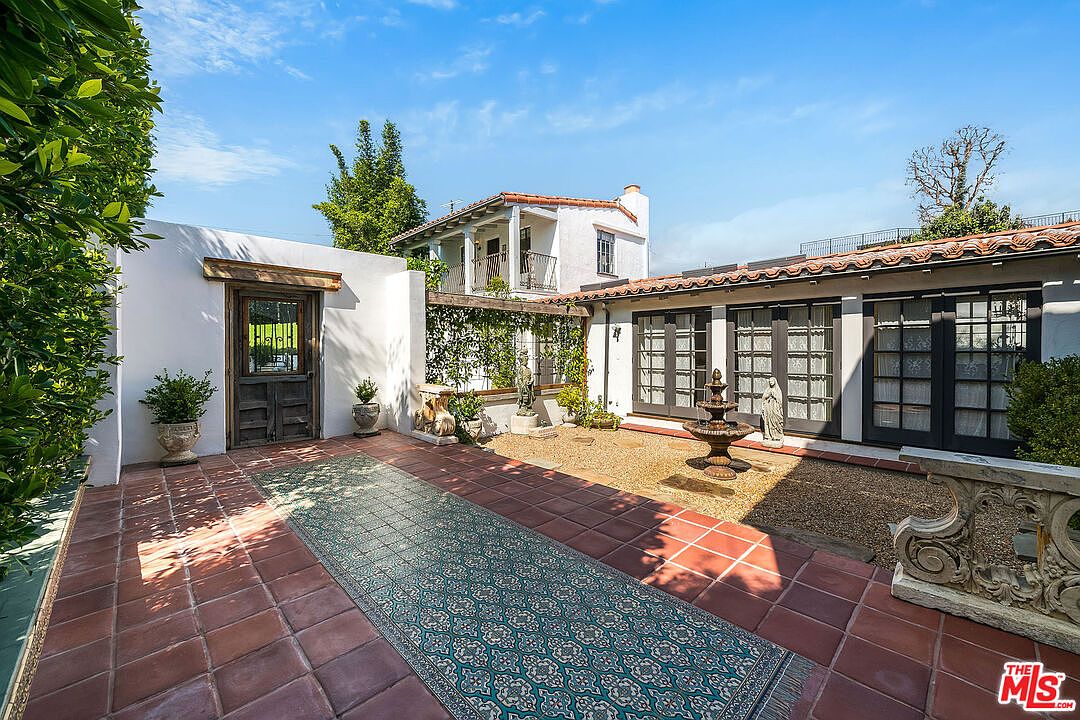 The interior courtyard at 1046 Chautauqua. A central stone fountain on a tiled mosaic, framed by terracotta paving, French doors along three sides, and the two-story Spanish facade rising at the back.