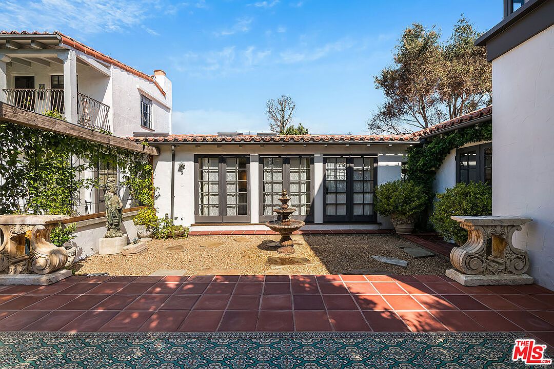 A second view of the courtyard at 1046 Chautauqua showing the wraparound French doors, the iron-railed second-floor balcony, and the central fountain at the heart of the plan.