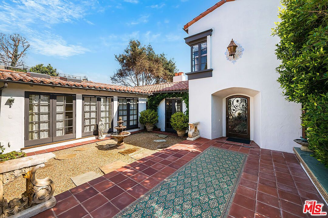 The arched entry door at 1046 Chautauqua, framed by white stucco and a wrought iron lantern. A patterned outdoor rug runs across the terracotta tile from courtyard to threshold.