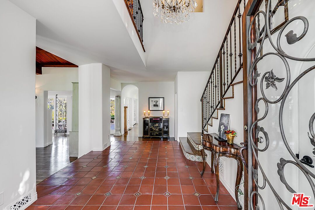 The two-story foyer of 1046 Chautauqua. A crystal chandelier hangs above terracotta tile inlaid with painted accents; a wrought iron stair rises to the right behind a tall ornamental gate.