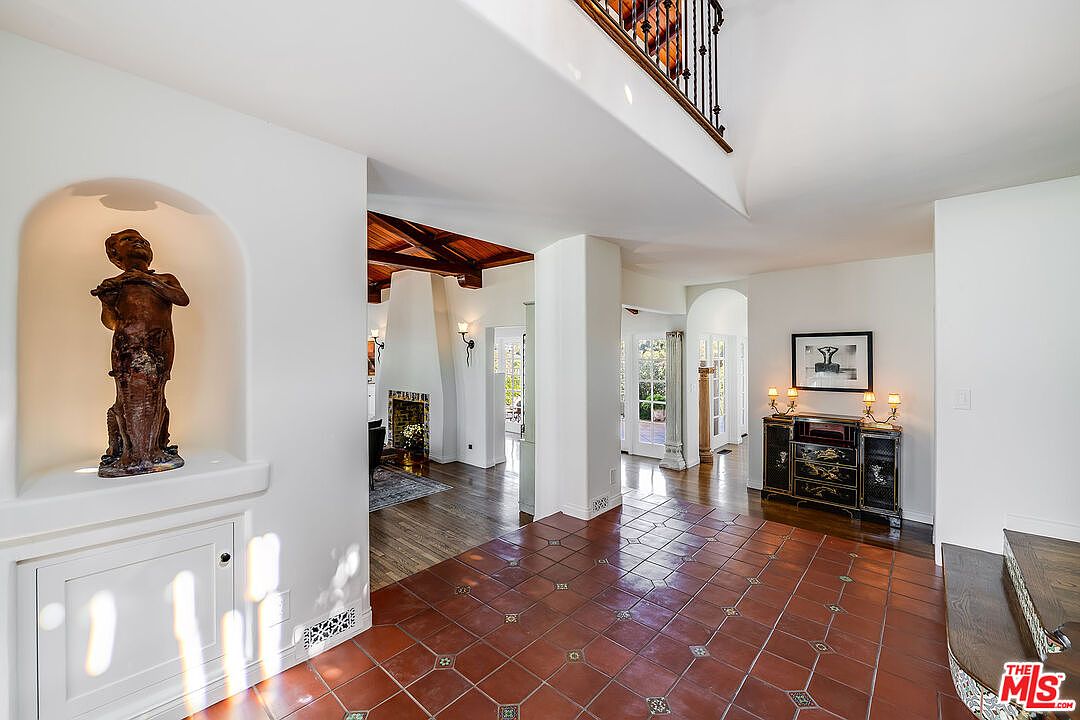 A view from the foyer through the great room at 1046 Chautauqua. A bronze statue niche sits to the left; the wood-beamed ceiling and stone fireplace are visible through the archway beyond.
