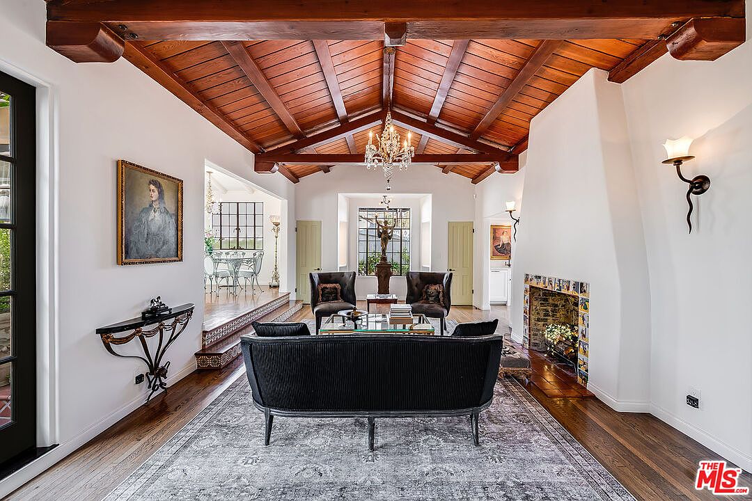 The reverse view of the great room at 1046 Chautauqua, showing the cathedral beams, the fireplace, the leaded glass French doors, a 19th century portrait above a console, and a long view through to the dining room beyond.