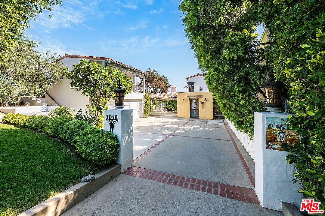 The gated entry of 1046 Chautauqua Blvd. A restored 1930 Spanish Colonial with white stucco and red clay tile roof, set behind ornamental gates above a courtyard driveway.